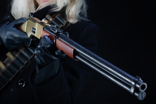 Old west blonde girl in black hat with gun on black background