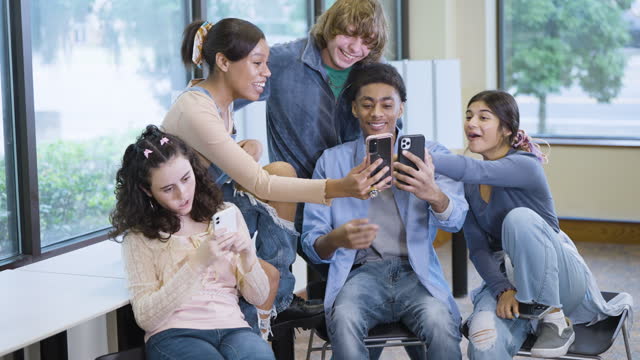 Multiracial teenagers smiling, looking at mobile phones
