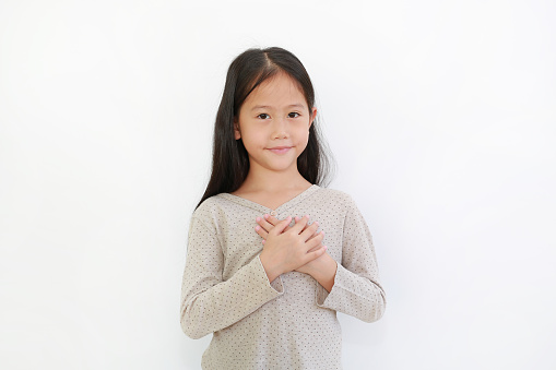 Portrait of Asian little girl holding hands on heart gesture of love. Kid place arms on chest isolated on white background.