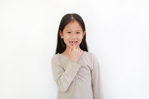 Portrait of smiling Asian little child girl with broken tooth and sucking finger in his mouth isolated on white background.