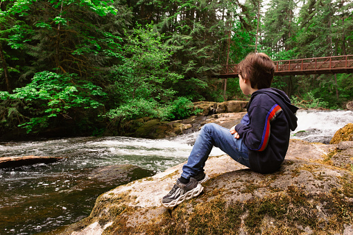 Boy Sitting on the Rive Bank Enjoying the View in Lacamas Regional Park, Washington, USA.