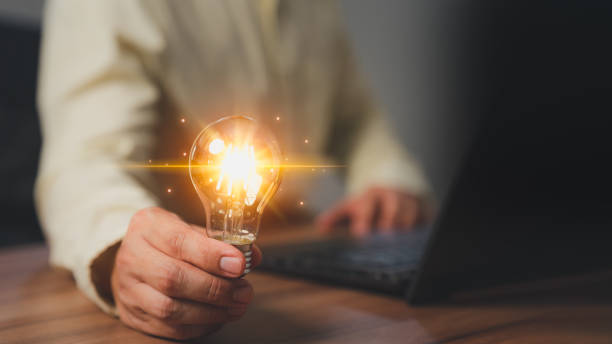 istock Man holding a light bulb while working on a computer laptop to think and generate new ideas through technological innovation and creativity. Idea inspired by online technology and innovation. 1500990443