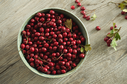 A bowl with hawthorn (Crataegus monogyna) red berries on rustic wooden table background