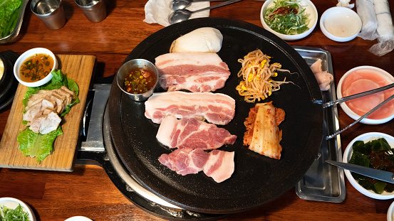 Pan-fried black pork meal in Jeju Korean restaurant, fresh delicious korean food cuisine on iron plate with lettuce, kimchi, banchan and sauce, lifestyle.