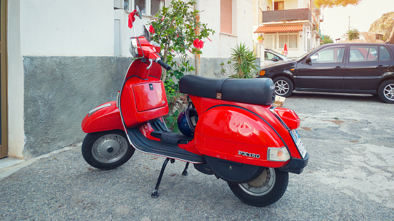 Tropea, Italy - September 10, 2019: Red Italian Vespa scooter parked near apartments, traditional transport in Italy.