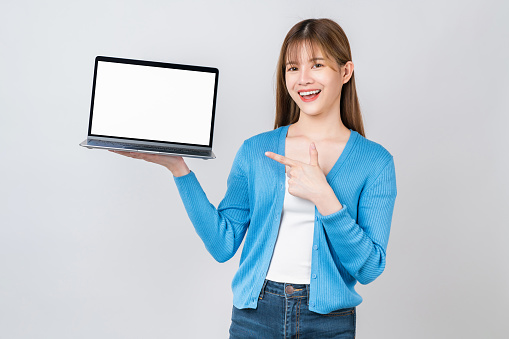 Cheerful beautiful Asian woman holding laptop on grey background.