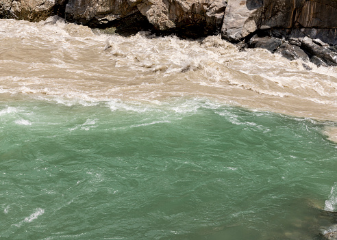 Muddy flood water and pure clear water flowing parallel with each other in the river swat closeup view