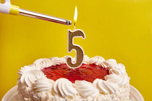 A candle in the form of the number 5, stuck in a festive cake, is lit. Celebrating a birthday or a landmark event. The climax of the celebration.