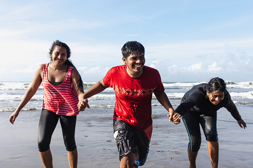 Happy latin friends teenagers at beach party runs and jumping to pacific ocean in Acapulco Mexico Latin America, hispanic people