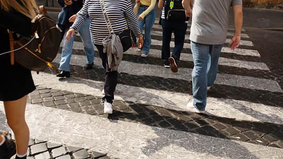 Rome, Italy - October 12, 2022. Zebra crossing. Legs of a crowd of busy pedestrians crossing a street.