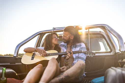 Young couple having fun with guitar on a pick-up truck during the summer road trip