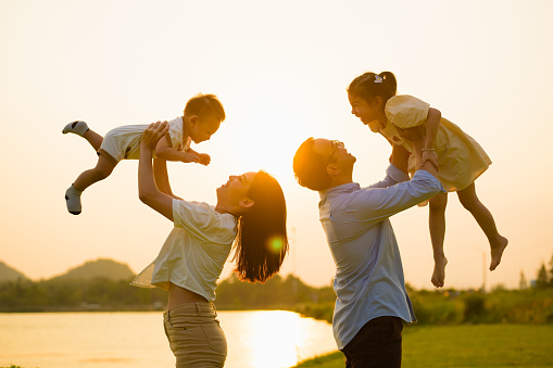 Father and mother holding children playing together in park in evening with sunset view, Cheerful family father mother and children enjoying picnic at park, Family with healthy lifestyle, Life insurance