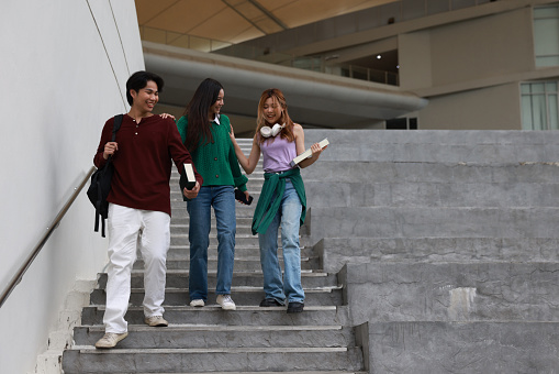 Two male and female students were walking down the university stairs. a young man holds a book and a young woman hold headphones on her neck. Education concept after finished class.