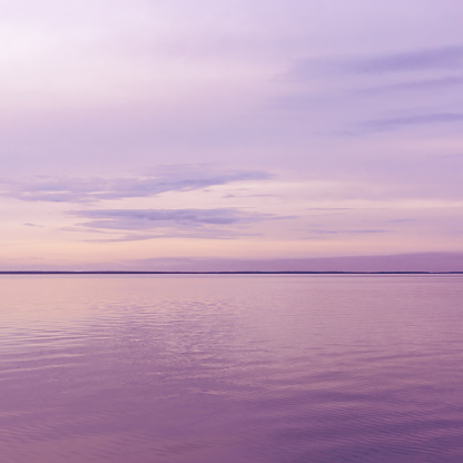 Colorful sky background on sunset or sunrise, purple pastel color clouds and surface water on lake Ik. Nature abstract composition with reflections on water, natural blue pink purple shades of skyline