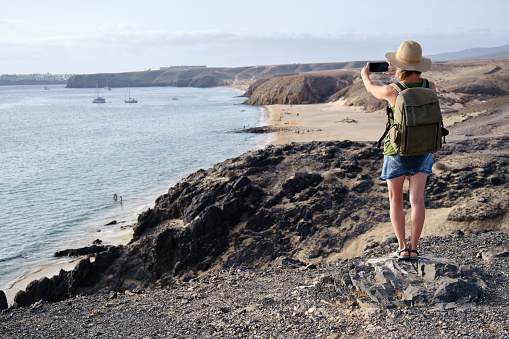 Tourist woman taking a picture from a cliff on the coastline in Lanzarote, Canary Islands.