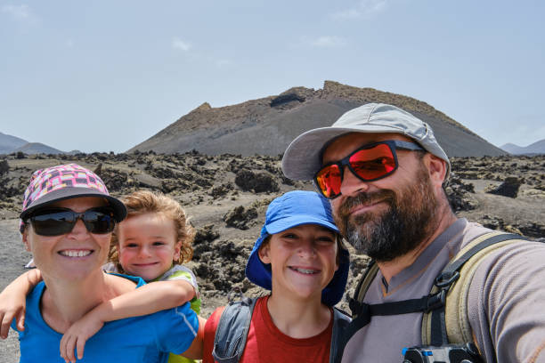 Family taking a selfie while hiking between volcanoes. El Cuervo volcano in the background. Lanzarote. stock photo