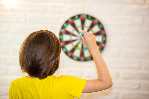 the boy holds a dart in his hand, he is going to throw it at the target, the child plays darts