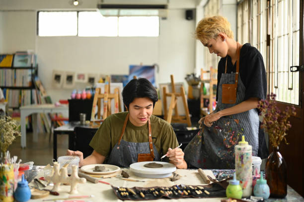 istock Smiling asian dressed in an apron shaping and scraping raw clay in the bright ceramic workshop. 1501056729