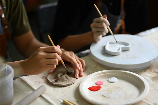 Cropped of two creative men painting pottery plate in workshop. Indoors lifestyle activity and hobbies concept.