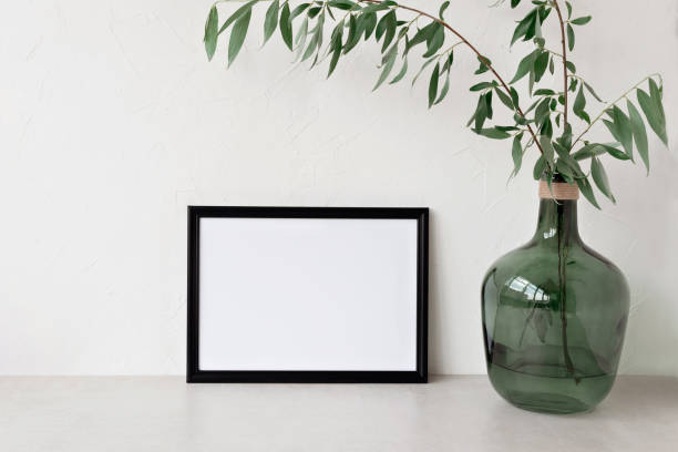 istock Empty black picture frame mockup, copy space, green glass vase with willow tree branches on beige tabletop and beige wall background. Minimalist art poster template, floral home interior decoration 1501056792