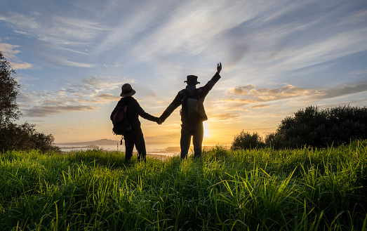 Couple holding hands and standing on Mt Eden summit at sunrise. Rangitoto Island in the distance. Auckland.