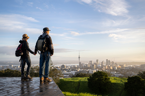 Couple standing on Mt Eden summit and watching sunrise over Auckland city. Selective focus on people in foreground.