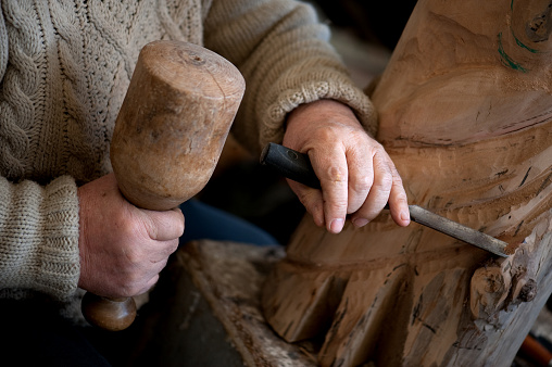 Hands of sculptor and hammer detail while carving.