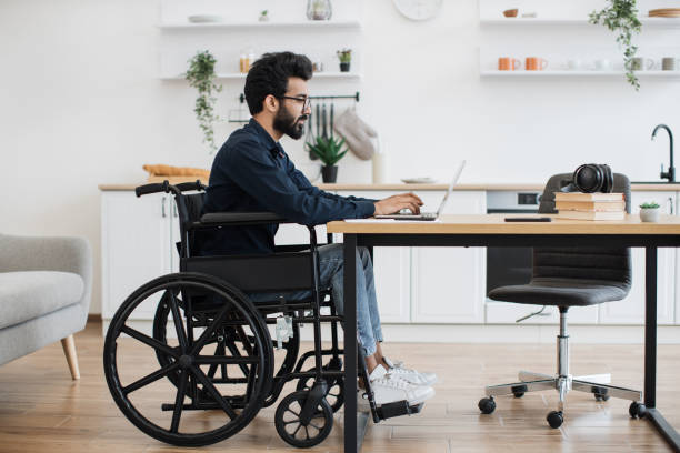 istock Male in wheelchair using laptop at desk in bright kitchen 1501059723