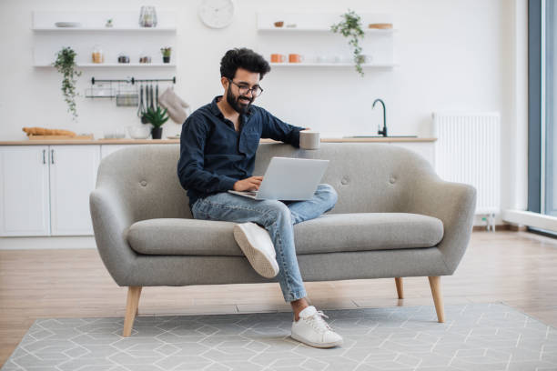 istock Person with tea and laptop resting on sofa in dining room 1501059816