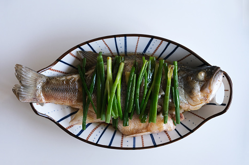 top down view of cooked steamed bass fish on white background. Chinese cuisine