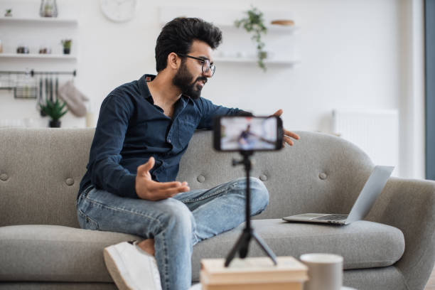 istock Indian man conducting live on phone and reading from laptop 1501063306