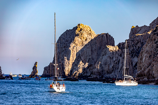 Boats sailing towards Cabo San Lucas Arch and Love Beach in the Sea of Cortez and the Pacific Ocean off the coast of the state of Baja California Sur of Mexico. Concept ships.