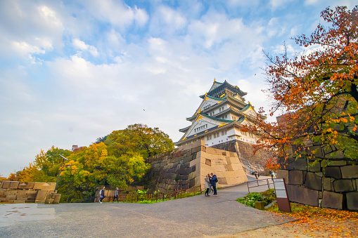 Osaka, Japan - November 11, 2017: Tourist taking pictures at majestic and beautiful Osaka Castle at dusk with trees around in autumn in Japan. Concept for heritage, Japanese kingdom, Shogun and Samurai Era.