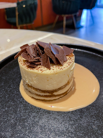 Stock photo showing close-up view of coffee flavoured, individual cheesecake dessert served in a restaurant in a pool of cream.