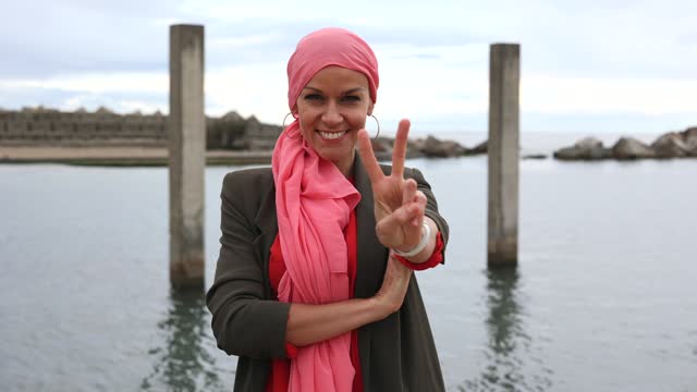 happy mature woman smiling with a pink scarf, symbol against breast cancer, - positive cancer fighter concept -