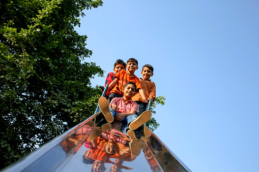 Group of elementary age children's of Indian ethnicity having fun on slide in the park together portrait close up with copy space.