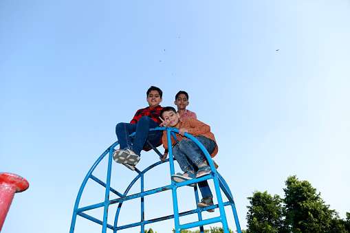Elementary children of Indian ethnicity playing portrait together in the park sitting on swing.
