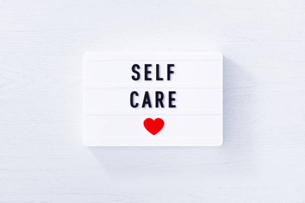 Self care written white lightbox on white wood background. Horizontal composition with copy space.