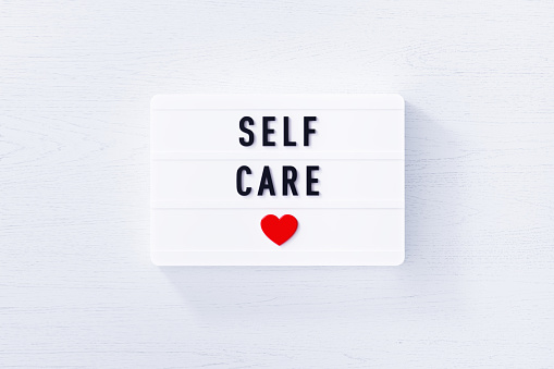 Self care written white lightbox on white wood background. Horizontal composition with copy space.