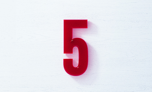 Number 5 made of glass on white wood background. Horizontal composition with copy space.