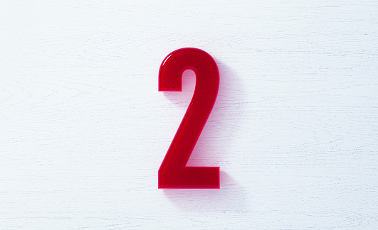 Number 2 made of glass on white wood background. Horizontal composition with copy space.