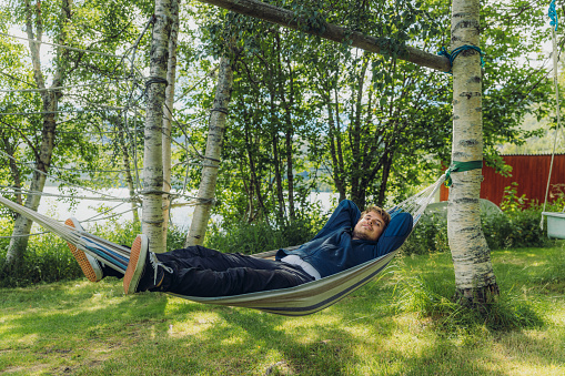 Side view of a male tourist contemplating sunny day in the green forest lying on the hammock and enjoying himself