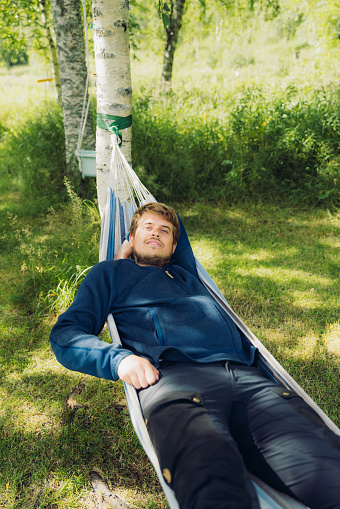Front view of a male tourist contemplating sunny day in the green forest lying on the hammock and enjoying himself