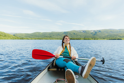 Portrait of a smiling female with long hair relaxing and canoeing in the lake with view of green forest in Nordland county, Northern Norway