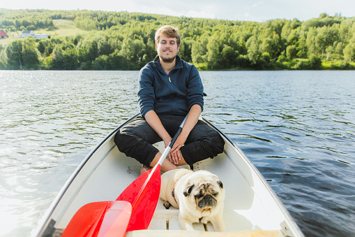 Front view of a male with relaxing pug canoeing in the lake with view of green forest in Nordland county, Northern Norway