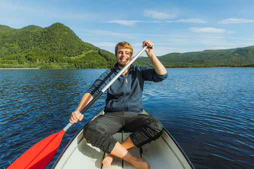 Portrait of a smiling male canoeing in the lake with view of green forest in Nordland county, Northern Norway