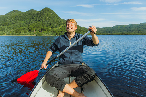 Young man rowing boat on a lake during a beautiful sunset. Travel, solitude, calmness and relaxation.