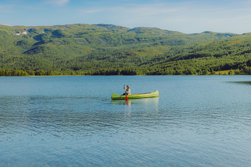 Female paddling a canoe on a pristine mountain lake at surise with her dog
