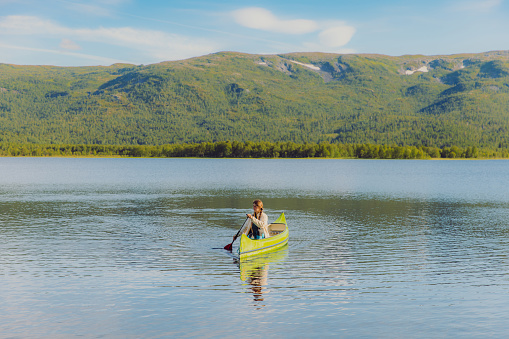 Side view of a female canoeing in the lake with view of green forest in Nordland county, Northern Norway