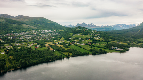 Drone high-angle photo of Volda city with two stadiums surrounded by the scenic green hills, snowcapped mountains and the lake in Western Norway, Scandinavia